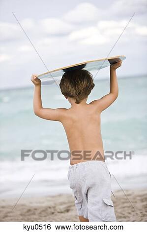 Stock Photograph - Rear view of a boy holding a body board over his head. Fotosearch