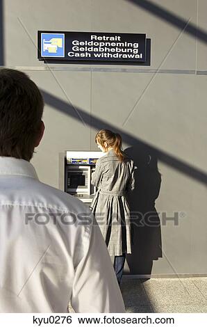 Stock Photograph - Rear view of a businessman looking at a businesswoman using an ATM. Fotosearch