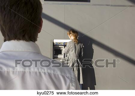 Rear view of a businessman looking at a businesswoman using an ATM View Large Photo Image Stock Photography - Rear view of a businessman looking at a businesswoman using an ATM. Fotosearch