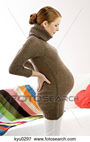 Stock Photo - Side profile of a pregnant young woman standing and looking at her abdomen. Fotosearch