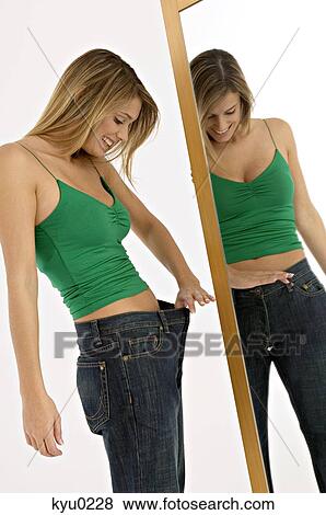 Stock Photo - Side profile of a young woman looking at her waist in front of a mirror. Fotosearch