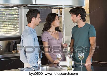 Stock Image - Three friends drinking wine in the kitchen. Fotosearch