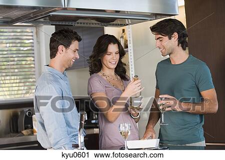 Stock Image - Three friends drinking wine in the kitchen. Fotosearch