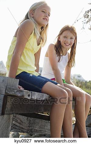 Two girls sitting on a boardwalk View Large Photo Image Stock Photo - Two girls sitting on a boardwalk. Fotosearch