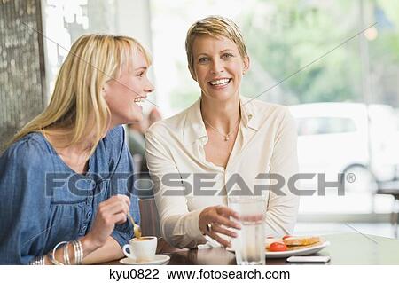 Stock Image - Two women sitting in a restaurant and smiling. Fotosearch