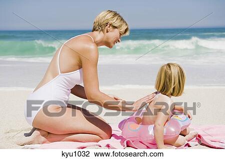 Stock Image - Woman applying suntan lotion on her daughter on the beach. Fotosearch