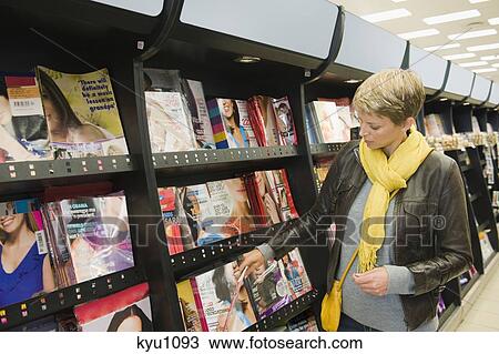 Stock Image - Woman choosing magazines in a supermarket. Fotosearch