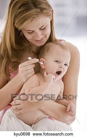 Stock Photo - Woman cleaning her daughter's ear with a cotton swab. Fotosearch