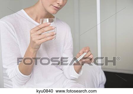 Stock Image - Woman holding a glass of water with a blister pack. Fotosearch