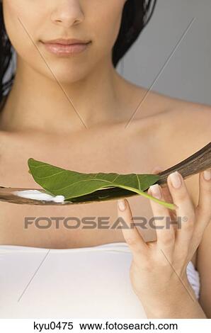 Stock Photography - Woman holding a leaf and moisturizer on wooden tray. Fotosearch