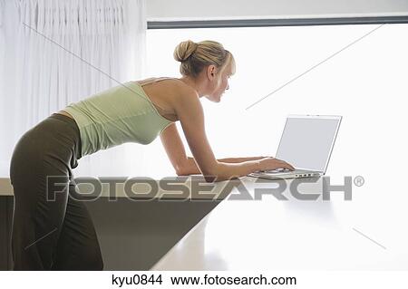 Woman leaning on a counter and working on a laptop View Large Photo Image Picture - Woman leaning on a counter and working on a laptop. Fotosearch