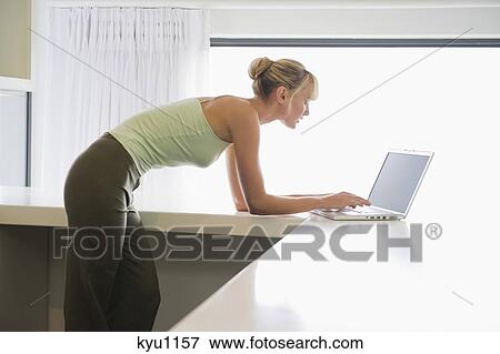 Woman leaning on a counter and working on a laptop View Large Photo Image Stock Photo - Woman leaning on a counter and working on a laptop. Fotosearch