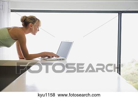 Woman leaning on a counter and working on a laptop View Large Photo Image Stock Photo - Woman leaning on a counter and working on a laptop. Fotosearch