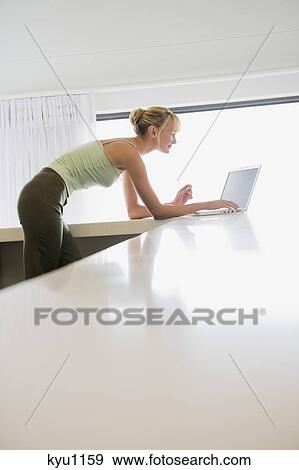 Woman leaning on a counter and working on a laptop View Large Photo Image Stock Photo - Woman leaning on a counter and working on a laptop. Fotosearch