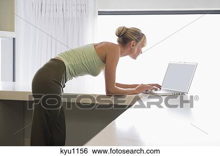 Woman leaning on a counter and working on a laptop View Large Photo Image Stock Photograph - Woman leaning on a counter and working on a laptop. Fotosearch