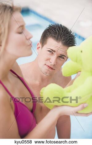 Stock Photo - Woman playing with a teddy bear and a man looking at her. Fotosearch