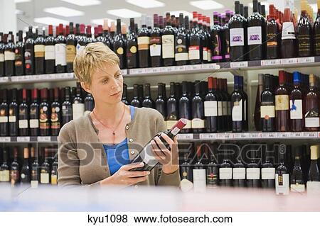 Stock Photo - Woman reading a label of a wine bottle. Fotosearch