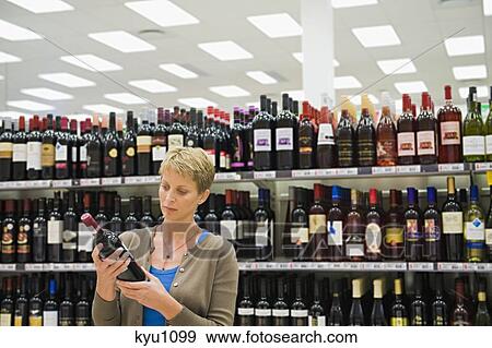 Stock Photo - Woman reading a label of a wine bottle. Fotosearch