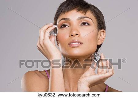 Stock Image - Woman rubbing ice cubes on her face. Fotosearch