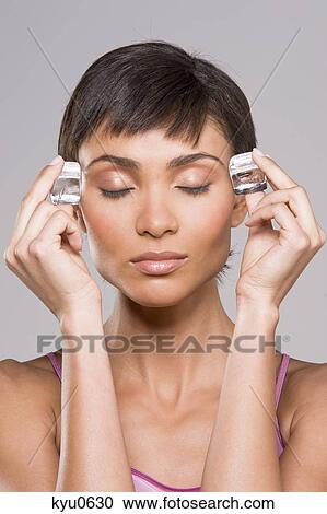 Stock Image - Woman rubbing ice cubes on her temples. Fotosearch