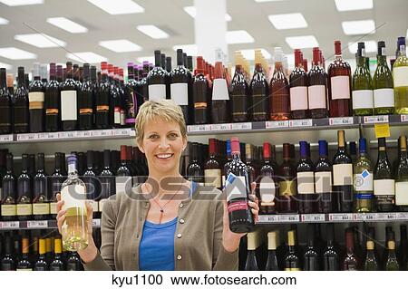 Stock Image - Woman showing two wine bottles in a supermarket. Fotosearch