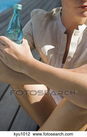 Woman sitting on a boardwalk and holding a water bottle View Large Photo Image Stock Image - Woman sitting on a boardwalk and holding a water bottle. Fotosearch