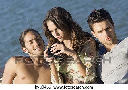 Woman sitting with two men and looking at a digital camera View Large Photo Image Stock Photography - Woman sitting with two men and looking at a digital camera. Fotosearch