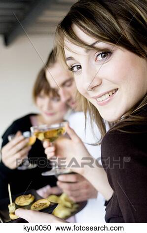 Stock Image - Woman smiling at the camera, holding glasses of champagne. Fotosearch