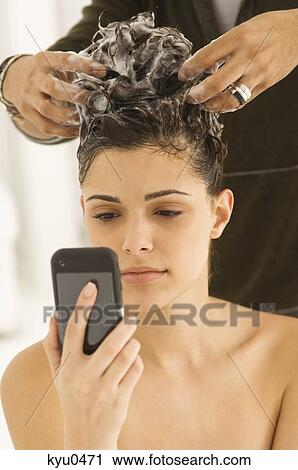 Woman using a mobile phone and having hair washed by a hairdresser View Large Photo Image Stock Image - Woman using a mobile phone and having hair washed by a hairdresser. Fotosearch