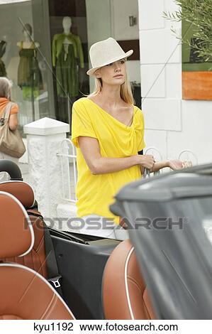 Stock Image - Woman walking towards a car after shopping. Fotosearch