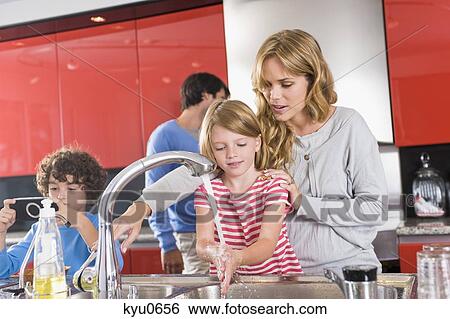 Stock Photograph - Woman washing hands of her daughter in the kitchen. Fotosearch