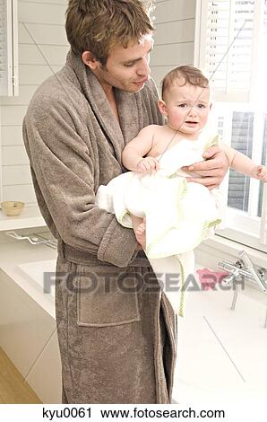 Stock Image - Young man in bathrobe with baby in bathroom. Fotosearch