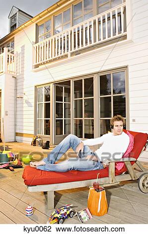 Young man with headphones lying on a deck chair View Large Photo Image Stock Image - Young man with headphones lying on a deck chair. Fotosearch