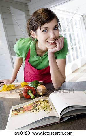 Young woman looking at recipe book, vegetables on a chopping board View Large Photo Image Stock Image - Young woman looking at recipe book, vegetables on a chopping board. Fotosearch