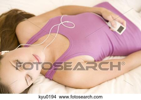 Picture - Young woman lying on bed, listening to music. Fotosearch
