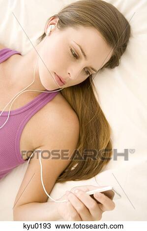 Young woman lying on bed, listening to music View Large Photo Image Stock Image - Young woman lying on bed, listening to music. Fotosearch