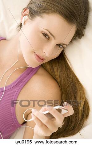 Stock Photography - Young woman lying on bed, listening to music. Fotosearch