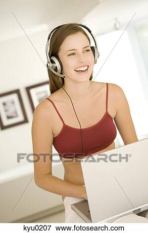 Stock Photo - Young woman smiling, listening to music with headphones, laptop on her knees. Fotosearch