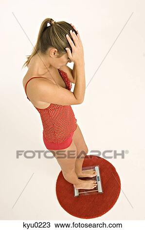Young woman standing on a bathroom scale with her hands on her head View Large Photo Image Stock Image - Young woman standing on a bathroom scale with her hands on her head. Fotosearch