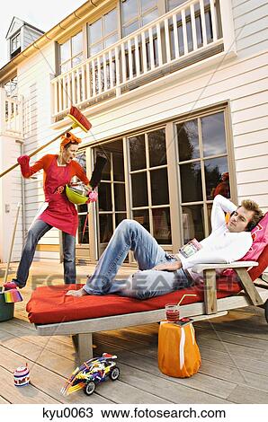 Stock Image - Young woman with cleaning accessories shouting at man lying on a deck chair. Fotosearch