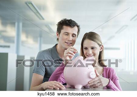 Stock Photo - Business executives inserting a coin into a piggy bank. Fotosearch