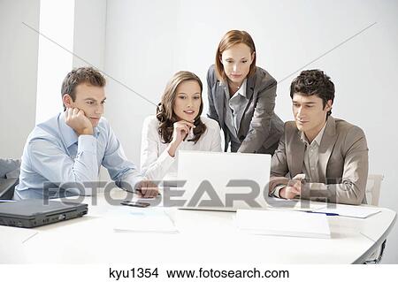 Business executives looking at a laptop in a board room View Large Photo Image Picture - Business executives looking at a laptop in a board room. Fotosearch