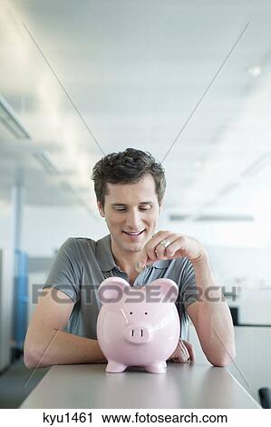 Stock Image - Businessman inserting a coin into a piggy bank. Fotosearch