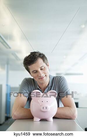 Businessman looking at a piggy bank and smiling View Large Photo Image Stock Photo - Businessman looking at a piggy bank and smiling. Fotosearch