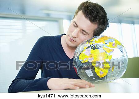 Stock Image - Businessman napping on a globe in an office. Fotosearch