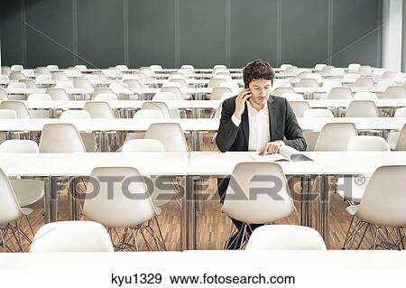 Businessman sitting at a cafeteria and talking on a mobile phone View Large Photo Image Stock Photo - Businessman sitting at a cafeteria and talking on a mobile phone. Fotosearch