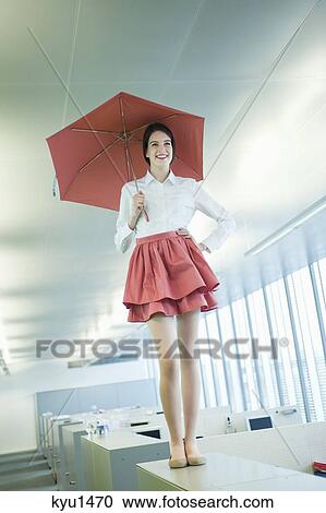 Businesswoman holding an umbrella and standing on a desk in an office View Large Photo Image Stock Image - Businesswoman holding an umbrella and standing on a desk in an office. Fotosearch