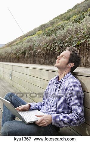Man using a laptop and listening to music View Large Photo Image Stock Photo - Man using a laptop and listening to music. Fotosearch