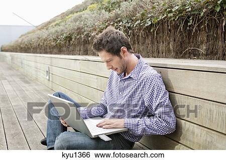 Stock Photograph - Man using a laptop on a boardwalk. Fotosearch