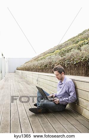 Stock Photography - Man using a laptop on a boardwalk. Fotosearch
